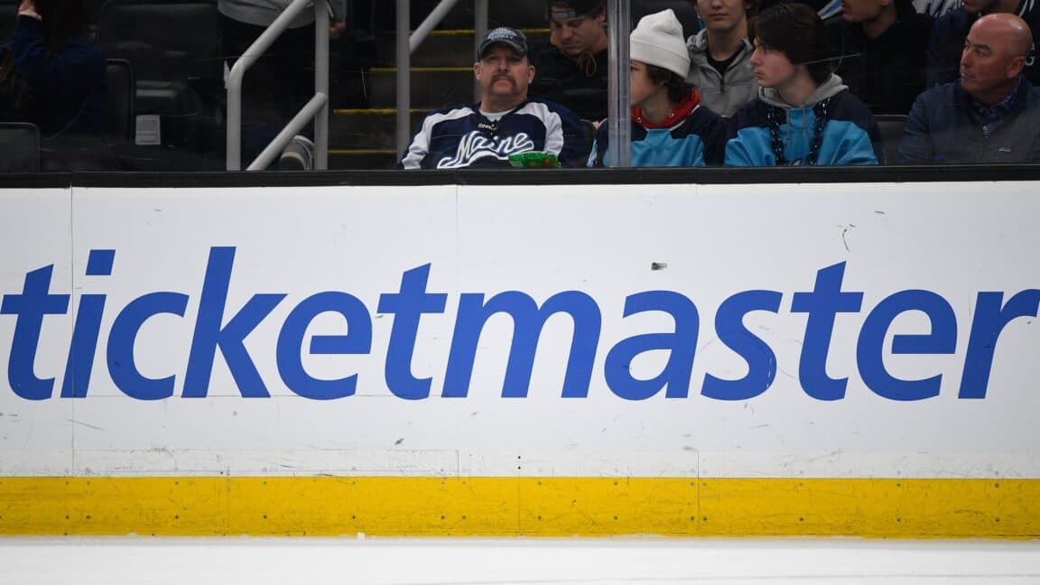 A large Ticketmaster logo on the boards inside an ice hockey arena.