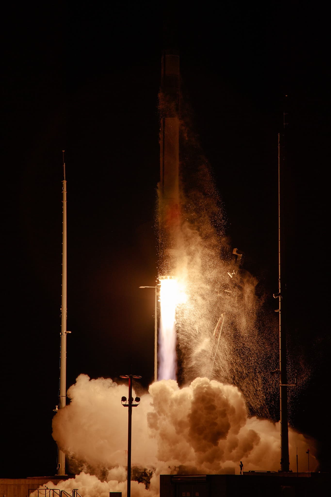A Rocket Lab HASTE rocket lifts off at night from NASA's Wallops Island, with bright orange and white flames illuminating billowing clouds of steam against a black sky.