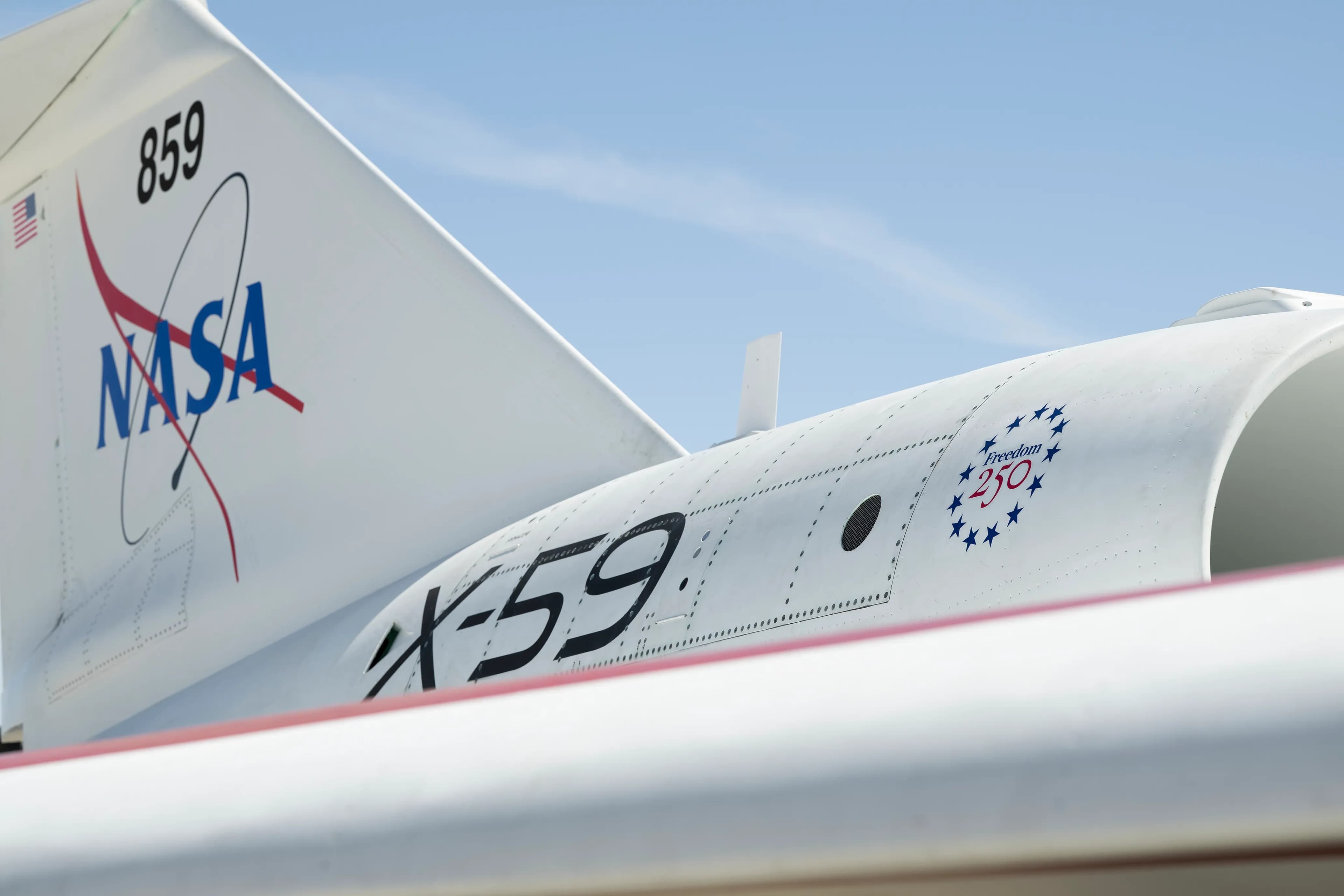 A close-up of NASA's X-59 tail showing a NASA graphic on the tail, X-59 on the side of the jet engine, and a Freedom 250 logo toward the front of the engine.