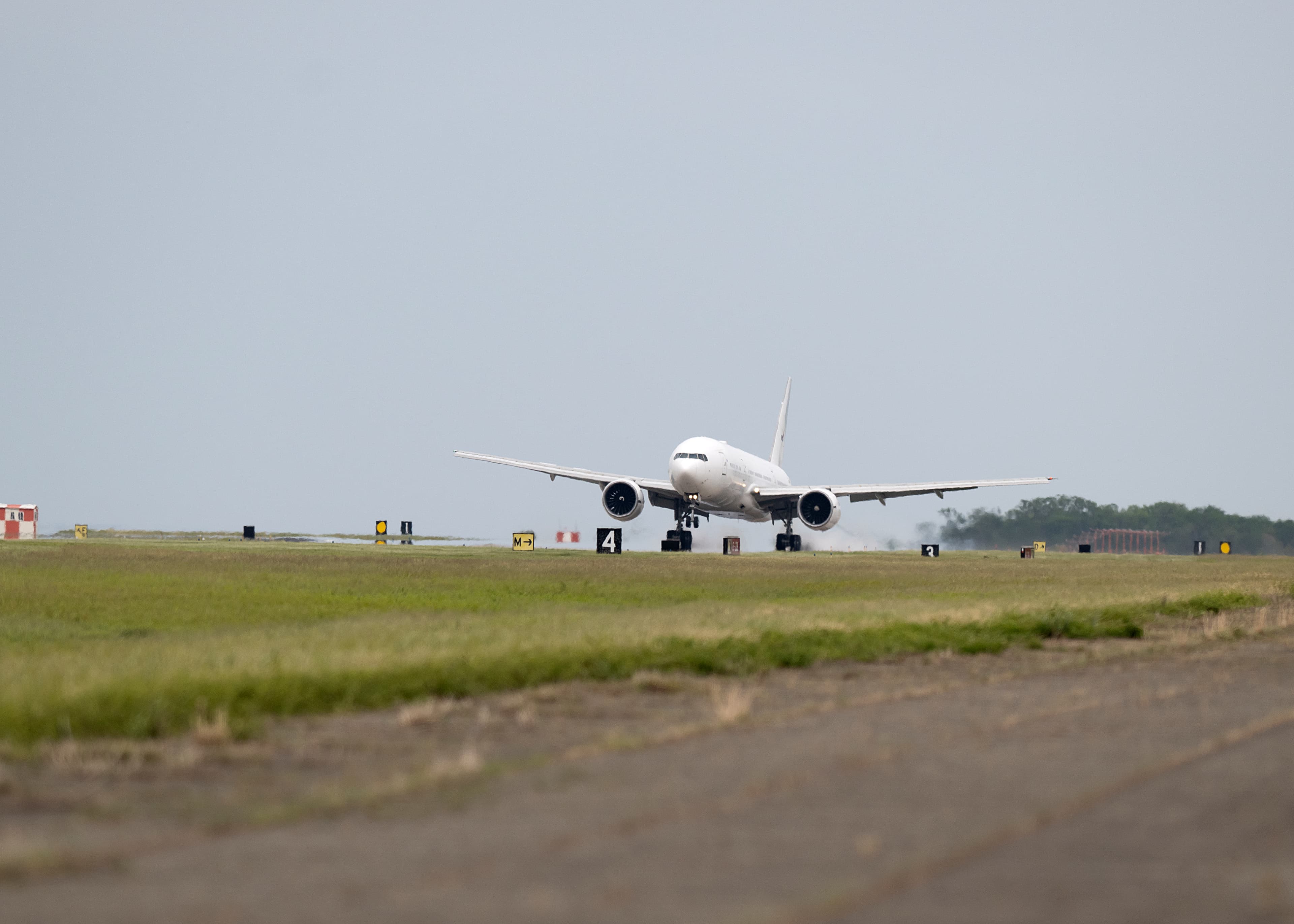 The white 777 aircraft can be seen touching down on a long runway with a row of grass along the pavement at NASA's Langley Research Center.
