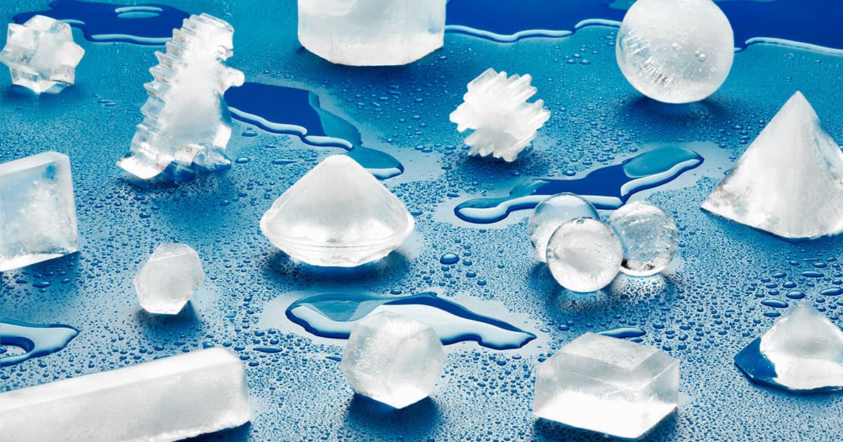 A photograph of ice cubes molded into different shapes—including a sphere, a snowflake, a diamond, and a dinosaur—scattered across a blue surface.