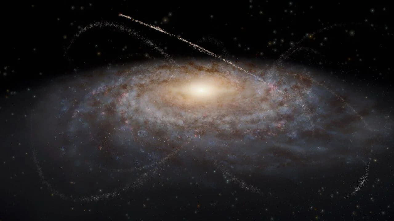 An artist’s impression of streams of stars around a galaxy. The galaxy occupies most of the image as a fuzzy blue-white oval with spiral features extending out clockwise. The light clouds are interspersed with small dark brown splotches in the same spiral pattern around the center, representing dust clouds. The galaxy’s center is a bright yellow glow. Overlaid on top of and surrounding the galaxy are several criss-crossing, faint tendrils of stars that represent satellite dwarf galaxies and star clusters that have been stretched out into long thin lines. The tendrils have various lengths and widths, though all are arcs rather than complete circles. The background is black.