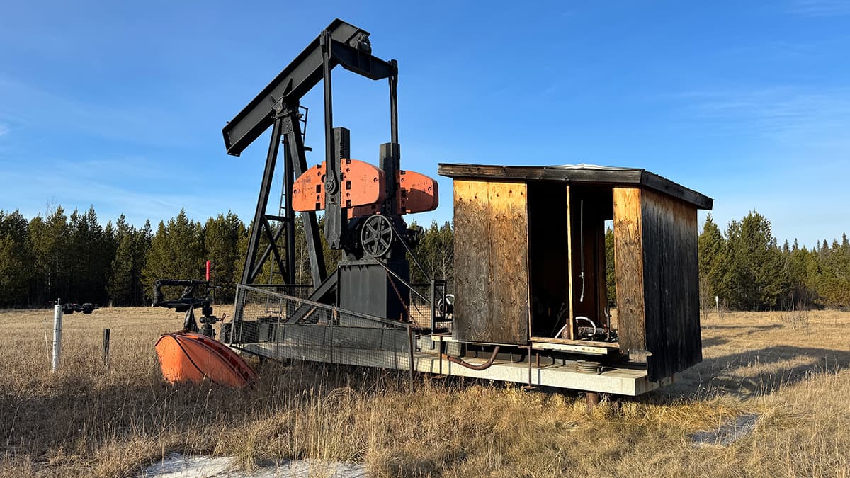 An old oil pump in a field of yellow grass with trees in the background (via eos.org)