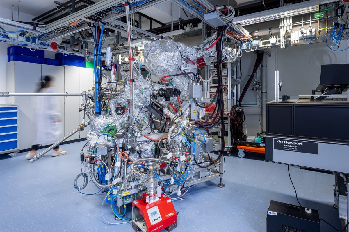 A woman in a lab coat is walking behind a technical device with lots of cables and metal parts. (via miragenews.com)